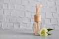 Aromatic reed freshener and flower on table against textured wall