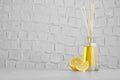 Aromatic reed freshener and lemon on table against textured wall