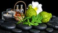 Aromatic spa of bottles essential oil in basket, fresh mint, rosemary, bergamot fruits, flower and candles on black zen stones