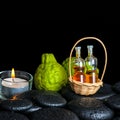 Aromatic spa concept of bergamot fruits, candle and bottles essential oil in basket on zen black stones with dew, closeup Royalty Free Stock Photo