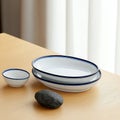 Arranged on a light wooden table is a set of white dishes with blue rims, encompassing a rectangular plate, a bowl, and Royalty Free Stock Photo