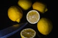 Arrangement of half lemons and whole organic lemons with a knife blade on a glittery black glass background Royalty Free Stock Photo