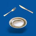 Arrangement made of levitating golden color fork, knife and plate. Dark blue background Royalty Free Stock Photo