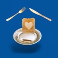 Arrangement made of levitating golden color fork, knife and plate with a slice of toasted bread with a heart shaped in the middle Royalty Free Stock Photo