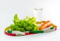 Carrot, green salad leaves and a glass of water surrounded by a measuring tape. Weight loss