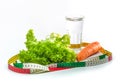 Carrot, green salad leaves and a glass of water surrounded by a measuring tape. Weight loss