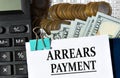 ARREARS PAYMENT - words on a white sheet against the background of a calculator, banknotes and pennies