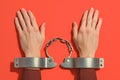 Arrested hands in handcuffs on vibrant red backdrop, law enforcement