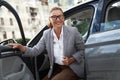 Arriving at the office. Portrait of attractive and happy business woman wearing eyeglasses getting out of her modern car