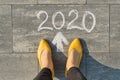 2020 arrow forward, written on gray sidewalk with woman legs, top view