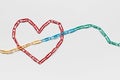 An arrow made from paperclips pointing upwards passing through a heart on a white background, shot from above, closeup Royalty Free Stock Photo