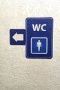 Arrow, pointer on blue plate of public male toilet signÃÂ± on plastered wall. Toilet sign. Restroom Concept .WC. Vertical shot. Royalty Free Stock Photo