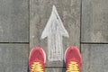 Arrow sign painted on gray sidewalk with women legs in sneakers, top view Royalty Free Stock Photo