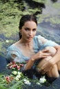 Art beautiful romantic woman lies in swamp in blue long dress with flowers. Portrait brunette in transparent dress in water swamp Royalty Free Stock Photo