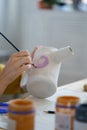 Art classes entertainment: artisan woman decorating potter jug with paint and paintbrush in workshop