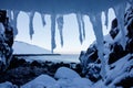 Art frame of white snow cold icicles on top foreground and stones beach of north arctic ocean with snowy cliff and mountain on the