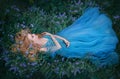 Art photo fairy tale sleeping beauty. Fantasy woman lies on blooming meadow in long blue medieval vintage dress. Summer Royalty Free Stock Photo