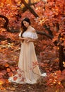Art photo fantasy woman queen standing in red autumn forest, white silk vintage old style dress. Girl princess beauty Royalty Free Stock Photo