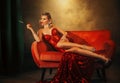 art photo happy woman lies on sofa fashion model posing bare long sexy legs high heels shoes red shiny dress. Retro girl Royalty Free Stock Photo