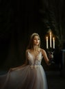 Art photo of medieval girl princess walks in dark gothic room. Woman queen is holding candlestick with burning candles