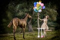 Beautiful girl with brown curly hair in wonderful dress ute posing smiling with colorful balloons and horse in fairytale forest Royalty Free Stock Photo