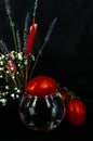 Art photo tomato on a glass of water with a bouquet of flowers on a black background Royalty Free Stock Photo