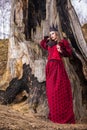 Art Photography Concepts. Mysterious Beautiful Fairy Medieval Princess in Red Dress and Spiky Black Crown in Forest in Early