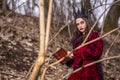 Art Photography. Mysterious Fairy Lady in Red Dress and Black Crown With Old Book. Posing in Forest Outdoors
