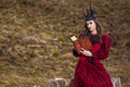 Art Photography. Mysterious Fairy Medieval Queen in Red Dress and Spiky Black Crown Posing With Ancient Book in Forest in Early