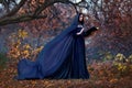 Art photography. Woman witch holds book in hands reads spell. Black clothes, cloak dress flies in wind. Fantasy girl elf