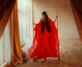 art Portrait real Fantasy girl arabic woman swinging on swing in room of full sand red long silk abaya dress. clothes Royalty Free Stock Photo