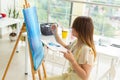 Art school, creativity and leisure concept - student girl or young woman artist with easel, palette and paint brush Royalty Free Stock Photo