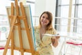 Art school, creativity and leisure concept - student girl or young woman artist with easel, palette and paint brush Royalty Free Stock Photo