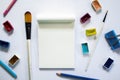 Art tools and blank notepad on white table. Painting art supply - brush, watercolor, pencil.