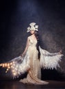 Art Woman angel with wings in luxurious long dress and fabulous headpiece. Girl bird with luminous wings posing on dark background Royalty Free Stock Photo