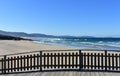 Wild beach with golden sand and wooden boardwalk. Blue sea with waves and foam, sunny day. Galicia, Spain. Royalty Free Stock Photo