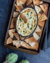 Artichoke dip on a baking sheet with various breads and pita triangles all around.