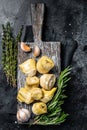 Artichokes hearts marinated with olive oil and herbs, pickled artichoke with garlic on wooden board. Black background