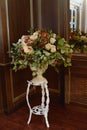 Artificial bouquet of flowers and berries in white antique vase near mirror.