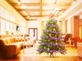 An artificial, Christmas tree with tinsel and stars stands on a blurred background of the hall with a large sofa. Bright