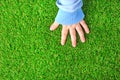 Artificial grass background. Tender hand of a baby on a green artificial turf.