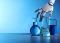 Artificial intelligence. Robot hand and laboratory glassware with liquids on table against light blue background, space for text Royalty Free Stock Photo