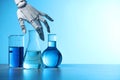 Artificial intelligence. Robot hand and laboratory glassware with liquids on table against light blue background, space for text Royalty Free Stock Photo
