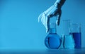 Artificial intelligence. Robot hand and laboratory glassware with liquids at table in blue light, space for text Royalty Free Stock Photo