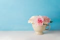 Artificial pink rose flowers in vintage cup on white and blue background