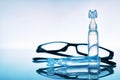 Lubricant eye drops with eye glasses and blue background composition Royalty Free Stock Photo