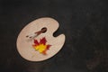 Artist Autumn. Multi-colored maple fallen leaf on a palette and brushes on dark background. Top view, close up, flat lay, place