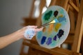 Artist hand holding paintbrush over oil paint mix on plastic palette closeup Royalty Free Stock Photo