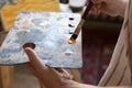 Artist holding rectangular palette, using paintbrush, blending paints