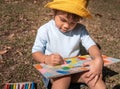 The artist little child girl sitting and painting in the recycling cardboard in a summer park